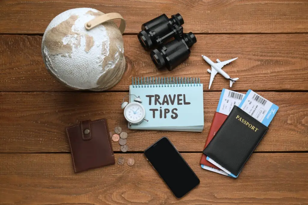 Notebook with phrase Travel Tips, smartphone and tourist items on wooden table, flat lay