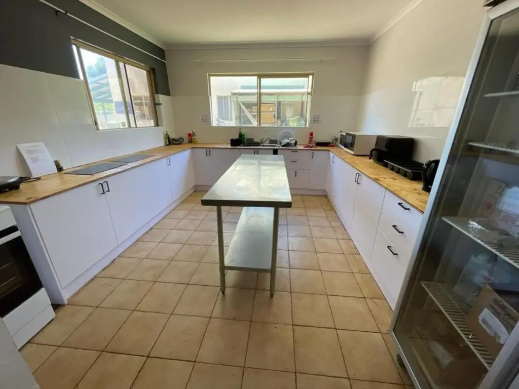 A large shared kitchen for guests and travelelrs with wodden and stainless steel benchtops, refrigerator, microwave and cook top at Kalbarri Backpackers Hostel