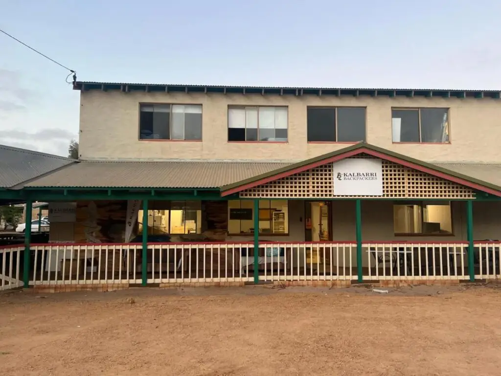 A street view of the location with picket fencc along the red desert land with the hostel close by in the background at Kalbarri Backpackers Hostel