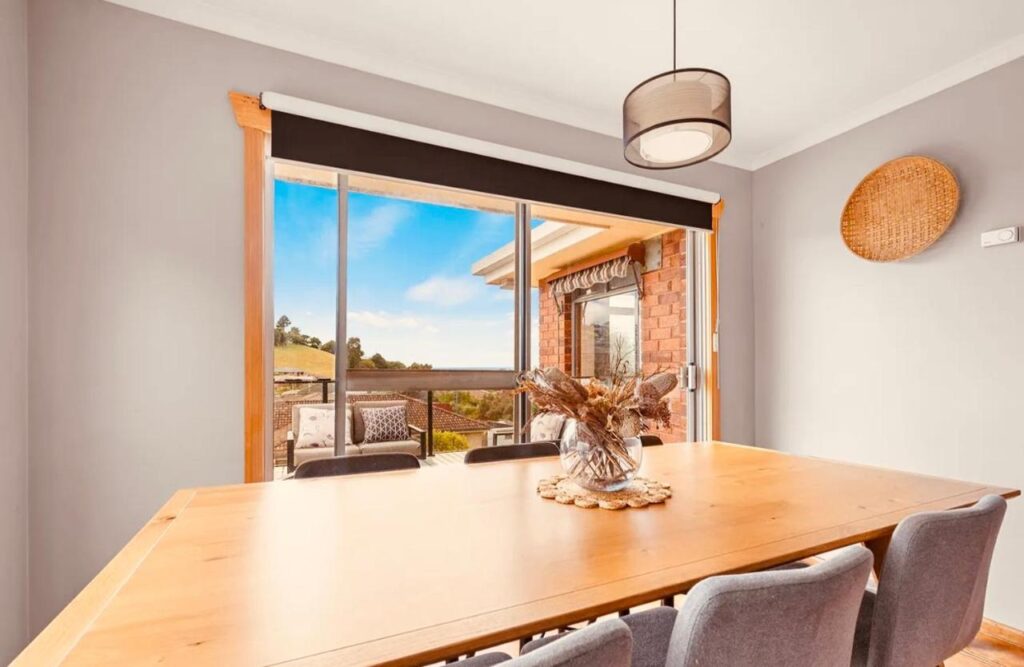 A dining room with wooden table and a view through a large window with sliding door to the balcony Natural & Relax House in Ulverstone