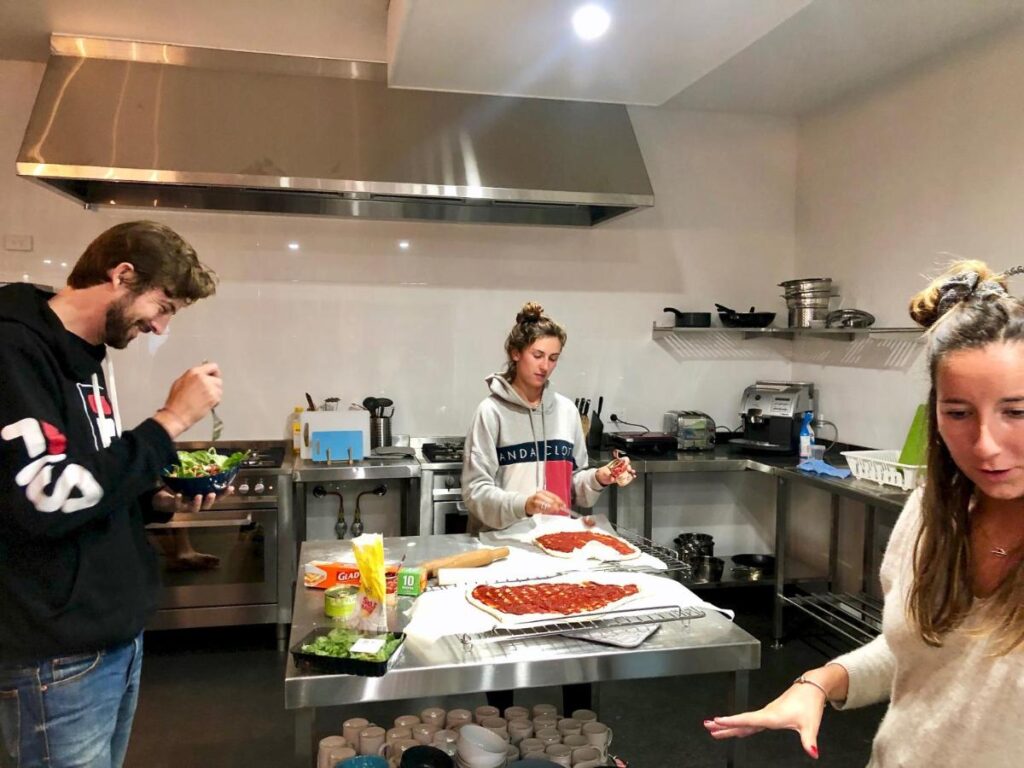 Travellers are making a pizza in the stainless steel shared kitchen at Spinners Backpackers