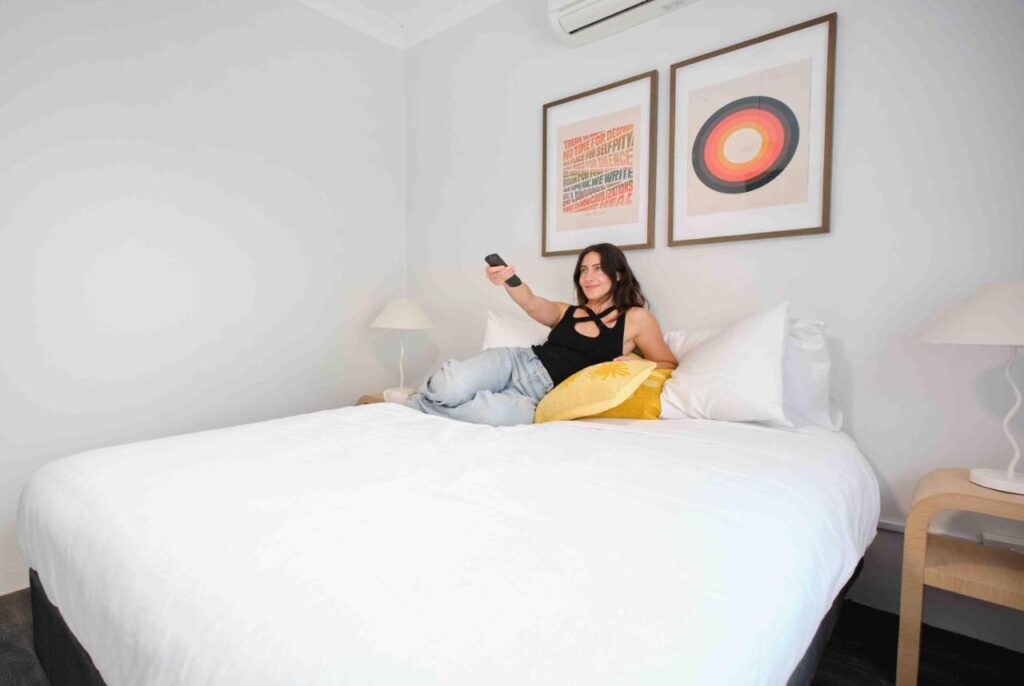 A fresh, modern private room with crisp clean bedding and a traveller checking whats on the television at The Village Surry Hills