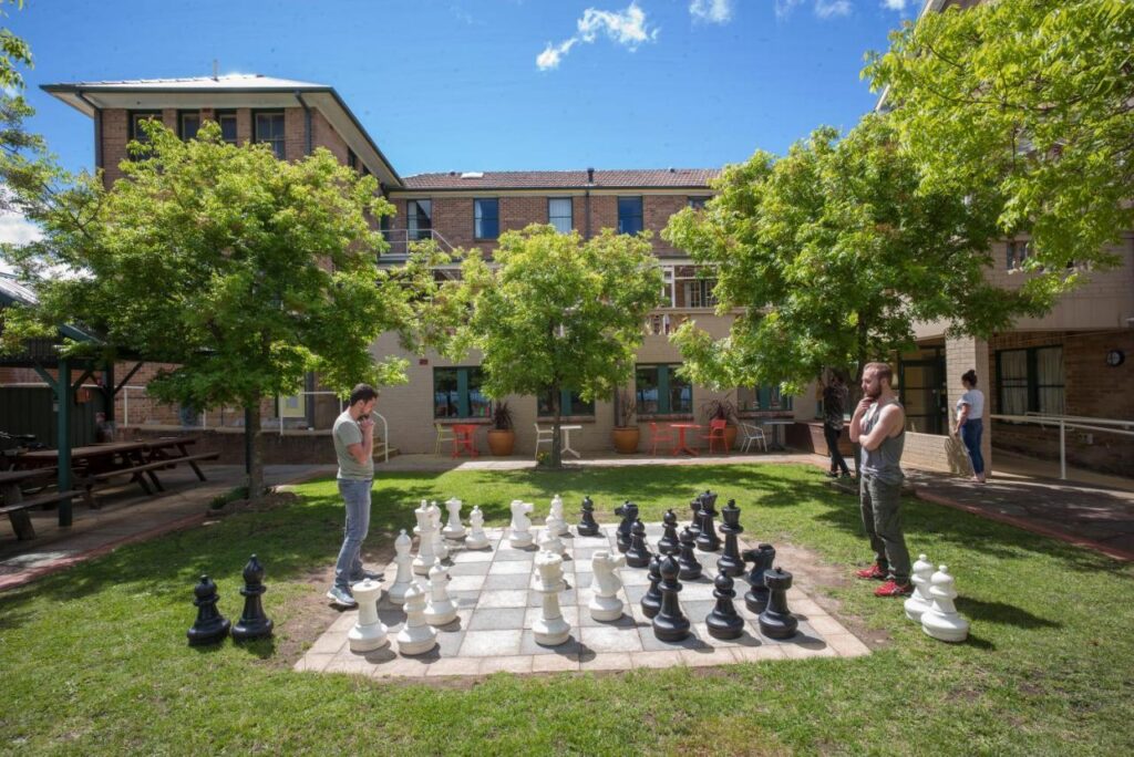 A couple of travellers playing a giant game of chess in the outdoor garden space at YHA Blue Mountains Katoomba